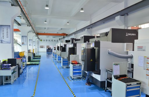 Rows of enclosed CNC machines along a blue-floored workshop.