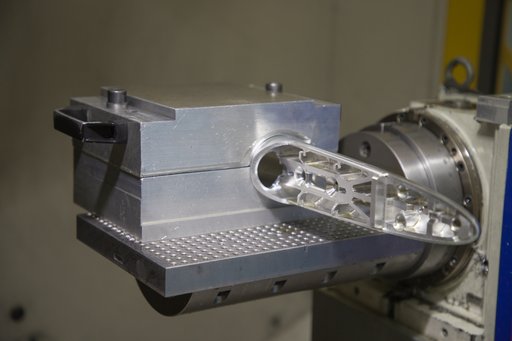A metal workpiece secured to a rotary fixture inside a machining enclosure.